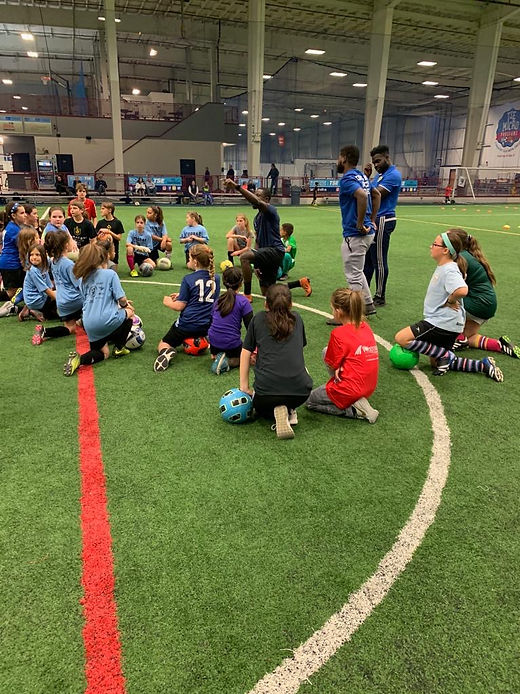 Youth players performing agility drills through yellow poles on an indoor field.