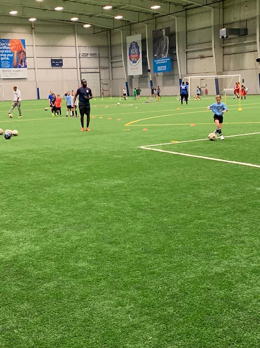 Coaches and a line of young players standing together on a soccer field marked with red lines.